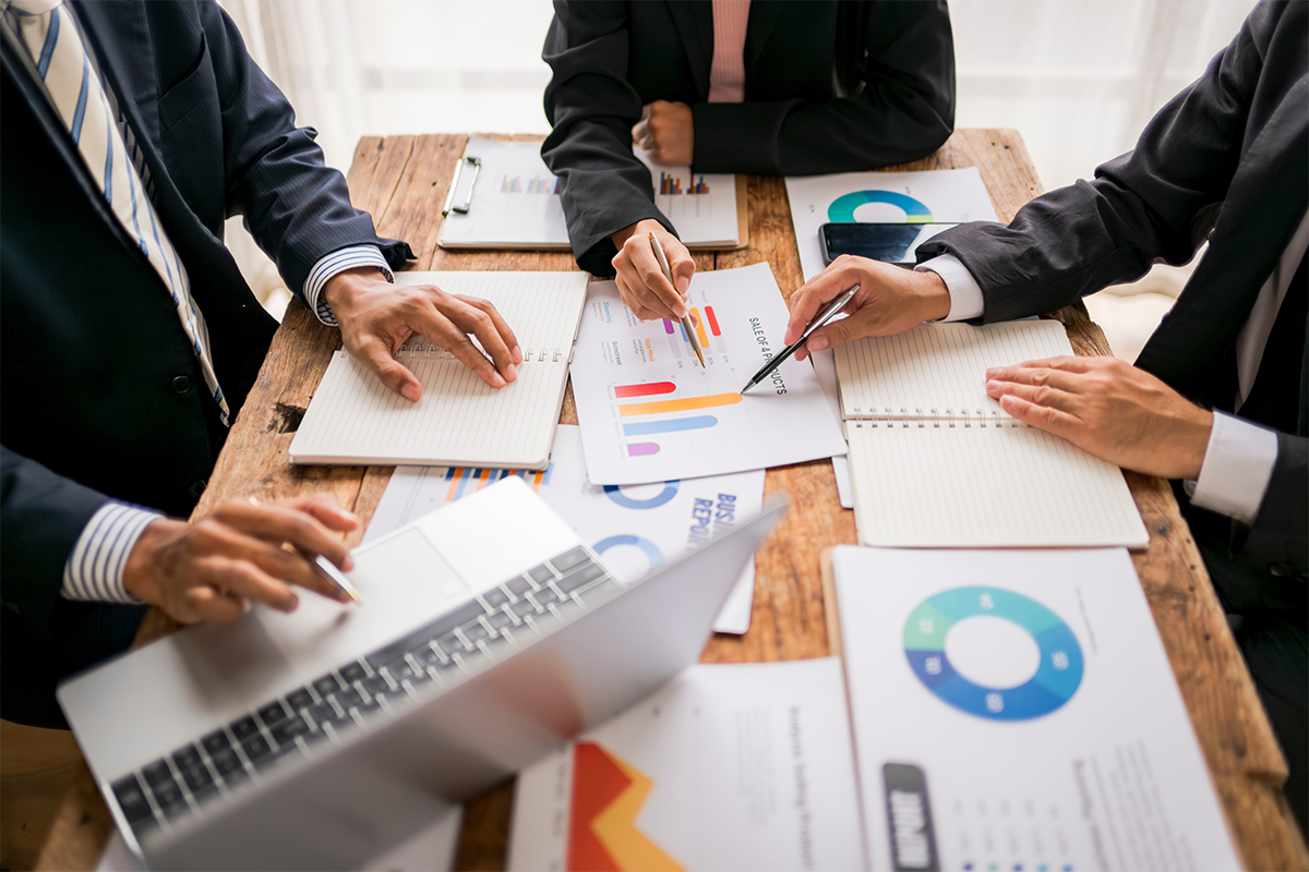 การประชุมทีมขายเพื่อตรวจสอบใบเสนอราคาและเอกสารรายงานการขายที่พิมพ์ออกมาจากระบบ Jubili CRM มีการใช้โน้ตบุ๊กประกอบการวางแผนและวิเคราะห์กราฟแท่งสรุปผลงานบนโต๊ะทำงาน